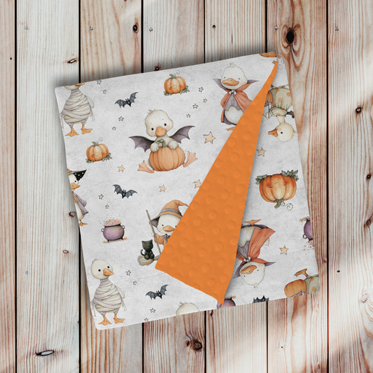doudou, couverture en minky avec endos en minky dot, à pois, texturé, ultra douce, motif halloween chez les oies avec endos orange papaye, avec oie blanche costumé, citrouille, fantôme, chauve-souris, momie, sorcière, chat noir, potion par 4Timini 
